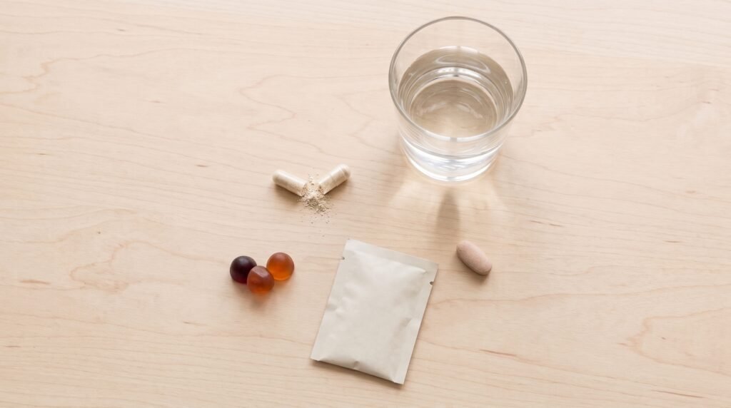 Cápsula de vitaminas prenatales abierta sobre yogur junto a gominolas y sobres en polvo para embarazadas